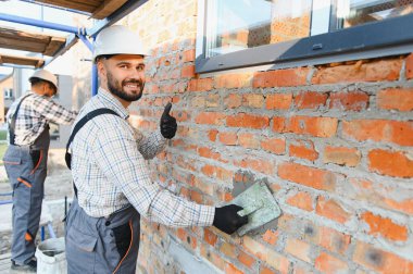 Profesyonel inşaat işçisi harici bir tuğla duvar inşa ediyor. Kaliteli iş için iyi niyet göstergesi.