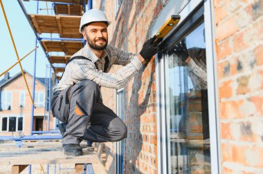 Bir inşaat sahasında pencere çerçevesini kontrol eden usta inşaat işçisi, hassas ve kaliteli kurulum garantisi veriyor