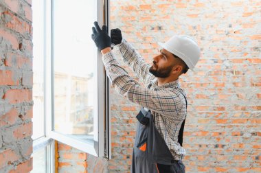 İnşaat işçisi sert bir şapka ve eldiven takıyor, tadilat altındaki bir binaya yeni bir pencere çerçevesi yerleştiriyor.