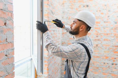 Sert şapkalı ve iş eldivenli genç bir adam pencere çerçevesi takıyor, evini yeniliyor.