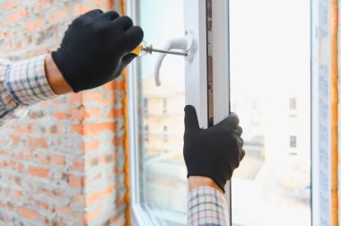 İşçi, ev tadilatı veya yenilenmesi sırasında beyaz bir pvc pencere çerçevesi ve bir tornavida kullanarak eldiven takıyor