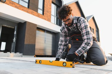 Genç adam yeni bir garaj yolu için kaldırım taşları kuruyor, ruhsal düzeyde bir araç ile bir seviye yüzeyi sağlama alıyor