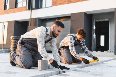 İki inşaat işçisi yeni bir veranda ya da garaj yolu için beton kaldırım taşı döşüyorlar.