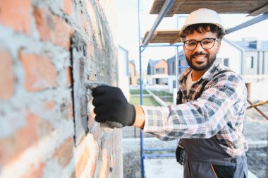 İnşaat işçisi, yeni inşaat alanına tuğla örgü örüyor, kameraya gülümsüyor.