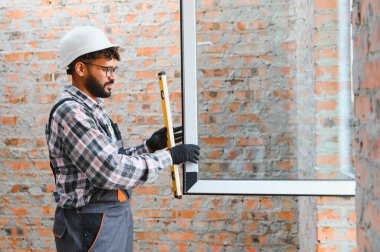 İnşaat işçisi, yeni bir pencere çerçevesini tuğla bir duvarın açılışına yerleştiriyor.