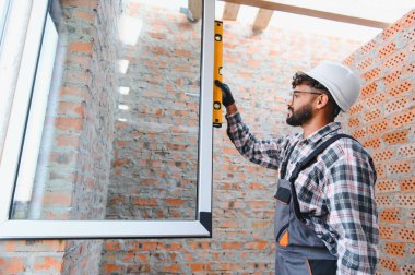 Profesyonel inşaat işçisi, tuğla bir duvarın içine yeni bir plastik pencere yerleştiriyor.
