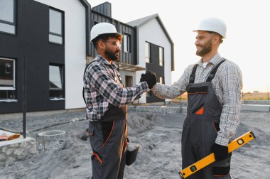 Takım çalışması ve işbirliği gösteren inşaat işçileri, güvenlik kaskı takarken konut inşaatına yumruk atanlar.