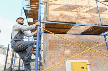 İnşaat işçisi, inşaat alanında inşaat işçisi, inşaat iskelesine tırmanıyor, ev inşaatını denetliyor.