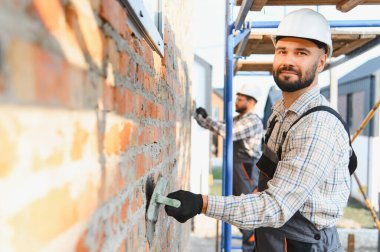 İki inşaat işçisi duvara alçı yapıştırıyor. İnşaat alanında malayla beton şekillendiren erkek inşaatçılar.