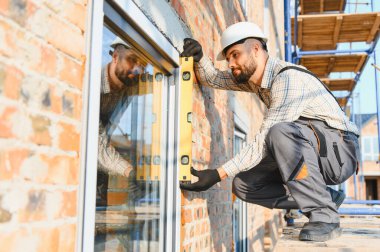İnşaatçı yeni bir pencere çerçevesi kuruyor, bir inşaat projesine kesin hizalama ve kalite sağlıyor