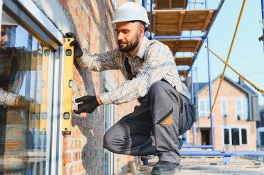 Bir evin ön cephesinde cam döşemesi için ruh seviyesini kullanan yetenekli bir inşaat işçisi. Doğruluğa ve yeni binaya odaklan