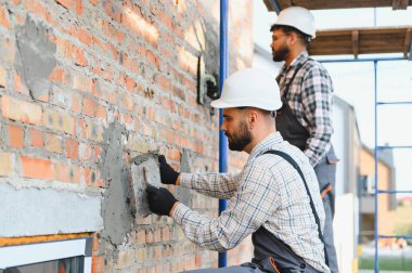 İnşaat işçileri tuğla duvar örüyor, yeni bir ev inşa ediyorlar. El işçiliğinin, işçiliğin ve yenilemenin vurgulanması