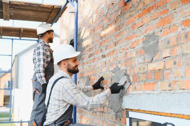 İnşaatçılar bir mala kullanarak duvara alçı yapıştırıyorlar. Tamamlanmamış bir binanın yenilenmesi ve geliştirilmesi