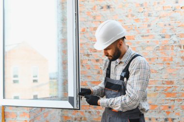 Becerikli inşaat işçisi, tadilat sırasında modern bir plastik pencere çerçevesini tuğla bir duvara dikkatlice yerleştiriyor.