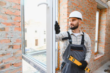 Erkek inşaat işçisi, bir inşaat sahasına yeni bir pencere çerçevesi kurarak, ruh seviyesine uygun bir hizalama sağlıyor