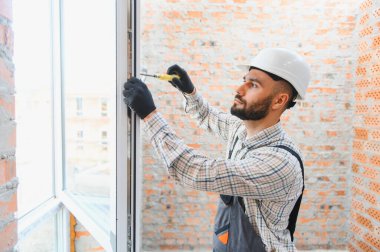 Yeni bir pencere tamir eden, ev yenileme ve bakım işleri yapan, sert şapka ve eldivenli inşaat işçisi.