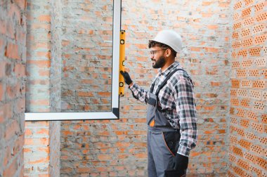 Profesyonel inşaat işçisi bir pencere kuruyor, yeni inşa evindeki bir seviyeyle hizasını dikkatlice kontrol ediyor