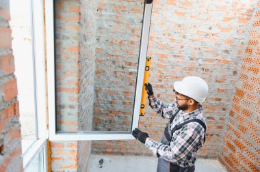 İnşaat işçisi, mükemmel hizalama ve kalite inşaatı için ruh seviyesini kullanarak yeni pencereyi dikkatlice kurar