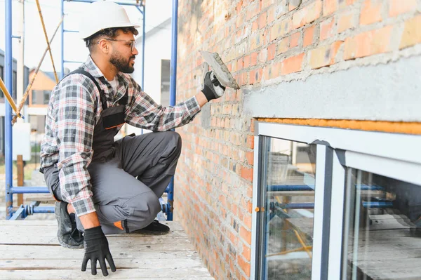 Kaliteli bir işçi iskeledeki malayla tuğla duvara sıva yapıştırıyor. Yenileme, işçilik ve sıkı çalışma kavramı.