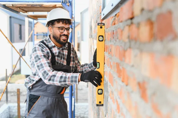 Tamamlanmamış tuğla bir duvarda ruhsal seviye bir alet kullanan profesyonel inşaatçı, inşaat sırasında hassasiyet ve kaliteyi sağlama alıyor