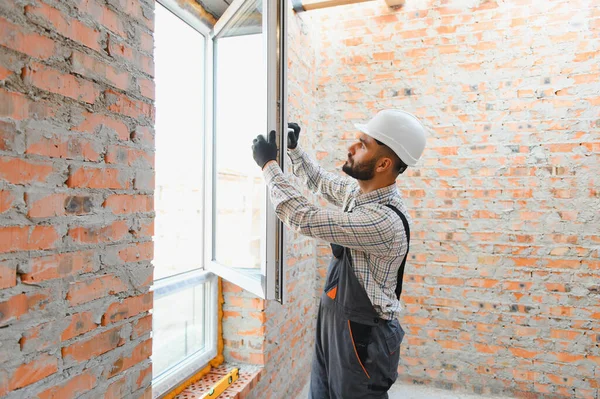 Yeni, modern bir pencere çerçevesi takan inşaat işçisi, yenileme sırasında bir evi iyileştiriyor