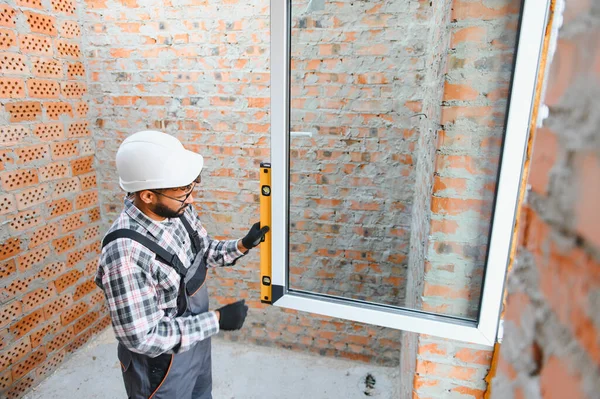 İşçi, yeni bir inşaat sahasında hassas kurulum sağlanarak, ruh düzeyinde pencere çerçevesini kontrol ediyor