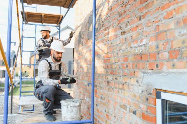 İnşaat işçileri tuğla bir duvara sıva uyguluyor, inşaat ve yenileme, inşaat iskelesinde birlikte çalışıyorlar.