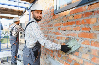 İnşaat işçisi, inşaat alanındaki bir malayla tuğla duvara havan topu atıyor.