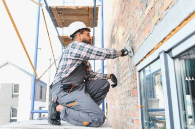 İnşaat işçisi tuğla bir duvara harç uyguluyor, bina yapıyor, yeni evi yeniliyor. İnşaat, işçilik, beceri ve güvenliğe odaklan