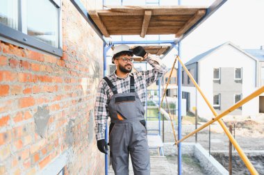Kasketli ve tulumlu işçiler iskeleye bakıyor, yeni bir inşaat alanına bakıyor. İnşa ve yenileme konsepti