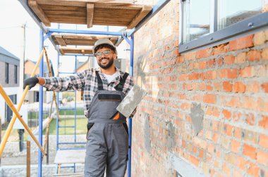 İnşaat alanında çalışan, elinde çimentoyla mala tutan, ev geliştirme ve yenilemeye katkıda bulunan mutlu bir adam.