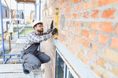 İnşaat işçisi inşaat alanındaki bir ruh seviyesini kullanarak tuğla duvarın dikey hizasını kontrol ediyor.