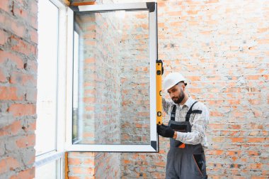 Tuğla duvar açıklığına yeni plastik pencere takan bir adam. Ev yenileme projesi sırasında inşaatçının güvenlik seviyesi