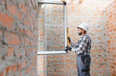 Tecrübeli inşaat işçisi ev yenileme sırasında tuğla bir duvara yeni bir pencere çerçevesi yerleştiriyor