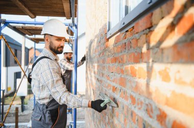 İnşaat işçileri yeni bir eve tuğla duvar örmek için havan topu takıyorlar.