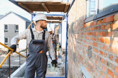 İnşaat işçileri inşaat iskelesinde tuğla döşüyorlar ve konut inşaatı, takım çalışması ve gün ışığında güvenlik duvarlarını onarıyorlar.