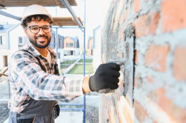 Yeni bir ev duvarına havan topu sürmek için mala binen mutlu müteahhit, kalifiye işçiliği ve ev inşaatını temsil ediyor.