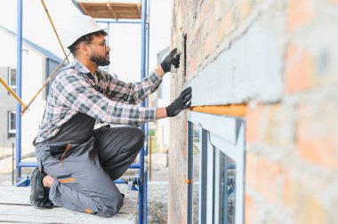 İnşaat işçisi, ev inşaatı sırasında yeni tuğla duvara alçı yapıştırıyor.