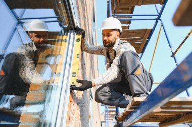 Profesyonel inşaat işçisi inşaat cephesindeki yeni pencere seviyesini iskeleden kontrol ediyor, kesin kurulum sağlanıyor