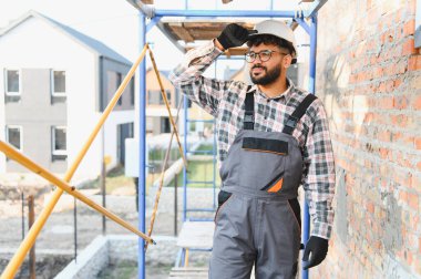 İnşaat alanındaki genç inşaatçı. Başlık ve tulum takıyor. Yeni konut projesini denetliyor.