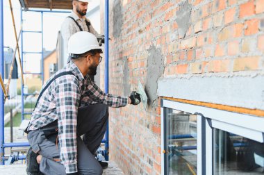 İnşaat işçileri inşaat iskelesinde tuğla duvara sıva uyguluyorlar. Bir binanın dış duvarını yeniliyorum.