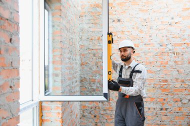 Profesyonel inşaat işçisi, tuğla bir duvarın açılışına yeni bir pencere çerçevesi yerleştiriyor.