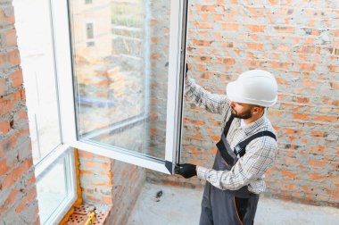 İnşaat işçisi, konutun yenilenmesi sırasında duvara çift camlı yeni bir pencere takıyor, odaklanmış ve ölçülmüş.