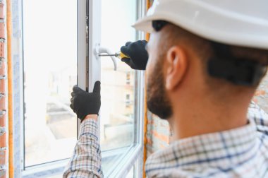 İnşaat işçisi evdeki daireye yeni PVC penceresi kuruyor. Pencere çerçevesini tamir eden tamirci, koruyucu eldiven ve şapka takıyor.