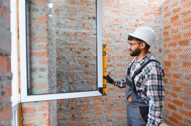 Ev tadilatı sırasında tuğla bir duvarda yeni kurulmuş bir pencere çerçevesinin işçi denetimi seviyesi