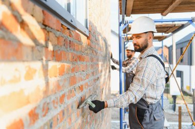 Profesyonel inşaat işçileri yeni bir ev için tuğla duvar örerek kaliteli taş işçiliği sağlıyorlar. Güvenlik ve takım çalışması
