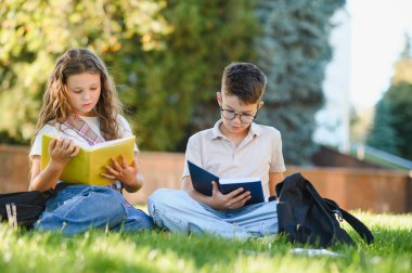 Okul çocukları yeşil çimlerde oturup ders kitapları okuyorlar. Okul dışında birlikte öğrenme ve çalışma. Eğitim kavramı