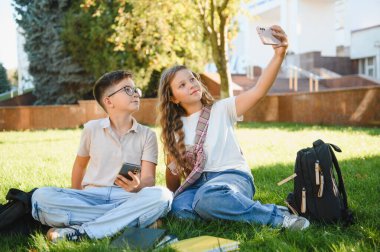 Genç öğrenciler akıllı telefonlarıyla selfie çekerek anılar yaratıyorlar. Okuldan sonra yeşil çimlerin üzerinde oturuyorlar.