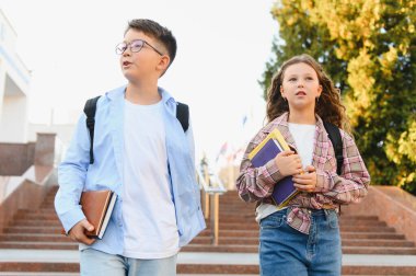 Okul çocukları kitap ve sırt çantası taşıyorlar, dışarıda yürüyorlar, akademik kurumda yeni bir eğitim deneyimi için hazırlar.