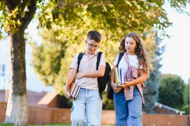 Okul çocukları kampüste birlikte yürüyorlar, sırt çantaları ve kitaplar taşıyorlar, eğitime hazırlar.